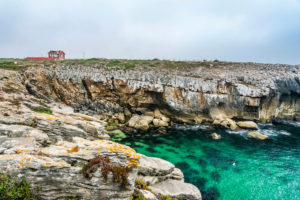 Europe, Portugal, Centro Region, Peniche Peninsula, bay with water in teal, lonely red house on the rocky coast Europe, Portugal, Centro Region, Peniche Peninsula, bay with water in teal, lonely red house on the rocky coast